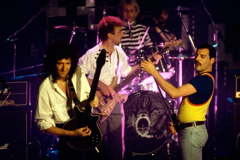 Queen in voller Besetzung auf der Bühne der Rose d’Or: Brian May, John Deacon, Roger Taylor und Freddie Mercury vor dem Wappen der Band.