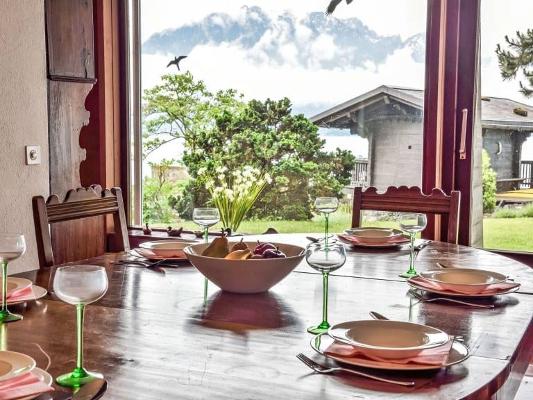Der gedeckte Tisch vor der Fensterfront, mit Blick auf Garten, Chalet und Berge.