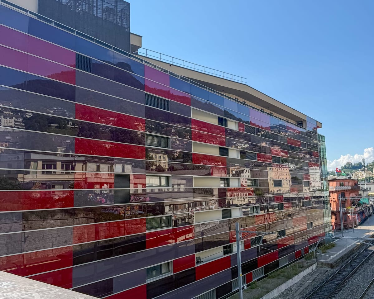 La facciata di vetro colorato del Freddie Mercury Hotel, ornata di vedute della vecchia Montreux, lungo i binari.