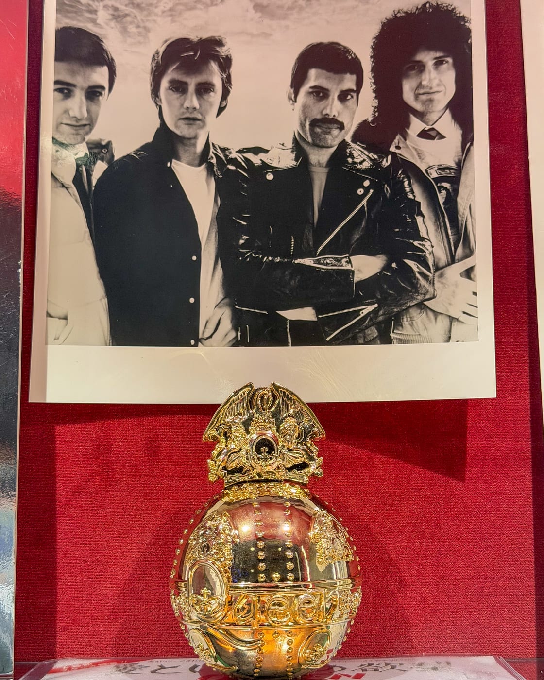 Ein Foto der Band und ein goldenes Objekt mit dem Queen-Wappen, dem von Freddie Mercury entworfenen Emblem.